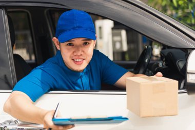 Asyalı genç kurye arabanın içinde üniforma giyiyor. Evrak tutanağı. Kapıdaki teslimat paketinin alınması için imzayı müşteriye teslim et.