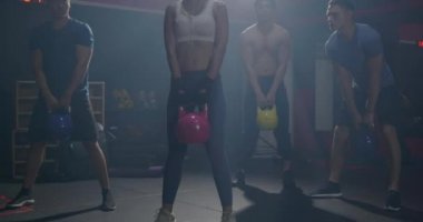 Spor salonundaki egzersiz sınıfında halterler üzerinde duran kaslı bir grup, genç erkek ve kadın kilolu kettlebell formundaki sporla sağlıklı yaşam stili egzersizleri yapıyor.