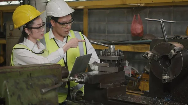 Asian professional mechanical engineer woman and operation man wearing uniform hardhat and goggles safety working on workshop metal lathe industrial manufacturing factory, Heavy industry lathe worker