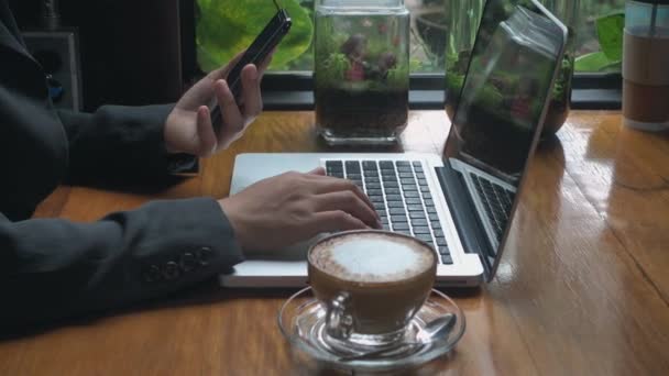 Επιχειρηματίας Κρατώντας Smartphone Και Πληκτρολογώντας Πληκτρολόγιο Στο Laptop Που Εργάζονται — Αρχείο Βίντεο