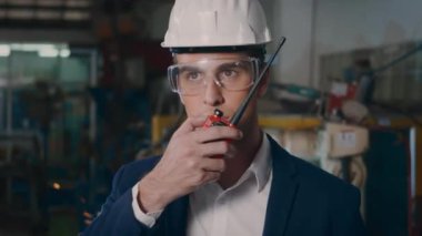 Güvenlik şapkaları ve gözlükleri takan profesyonel bir mühendis ağır bir endüstriyel tesiste elinde telsizle ateş kıvılcımlı bir robottan çelik kaynak yapıyor.