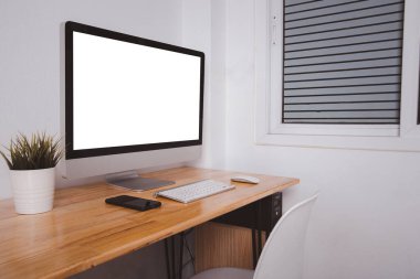 İş masasında beyaz boş ekranlı bilgisayar monitörü kablosuz fare, beyaz duvar arkaplanı üzerinde klavye, çağdaş ekipman çalışma alanı fotoğrafı