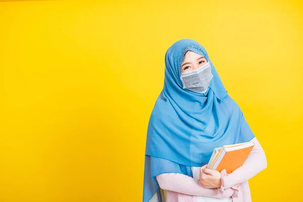 アジア系ムスリムアラブ人 若い女性の肖像宗教的な摩耗ベールヒジャーブと顔のマスク保護彼女は学生が手に本を保持するコロナウイルスを防ぐために 黄色の背景に孤立 大学に戻る — ストック写真