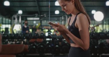 Aktif genç bir kadın spor salonu spor salonu spor salonu idmanından sonra akıllı telefon kullanarak oturmaya ara veriyor.
