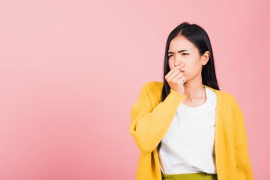 Asyalı, güzel, genç ve mutsuz bir kadın. Ne iğrenç bir koku. Burnu parmaklarıyla sıkıyor. Kadının kötü bir koku durumu var. Stüdyo çekimleri pembe arka planda, sağlık hizmetlerinde.
