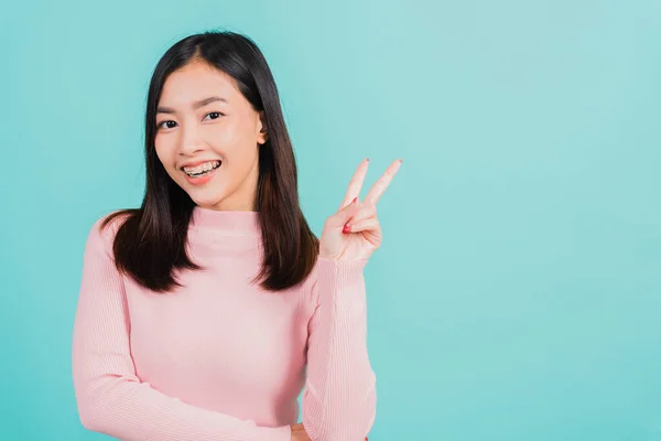 若いアジアの美しい女性の笑顔は 取り外し可能なブレースの後に保持し 青の背景に隔離されたVサイン勝利指を示す歯にシリコーン歯列矯正家臣を身に着けています 歯科衛生の概念 — ストック写真