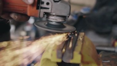 Elektrikli tekerlek kullanan işçi mengenedeki çelik yapıyı öğütüyor ve kesiyor üretim fabrikasındaki öğütme çarkından kıvılcım çıkıyor.