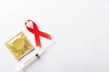 Kırmızı kurdele, HIV, AIDS kanseri farkındalığı, gölgeli kondom ve şırınga, beyaz arka planda izole edilmiş stüdyo çekimi, sağlık sigortası cinsel konsepti, Dünya AIDS Günü