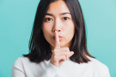 Dudaklarında işaret parmağı olan genç, güzel bir Asyalı kadın, sessiz bir kadın portresi, mavi arka planda izole edilmiş bir stüdyo çekimi, 
