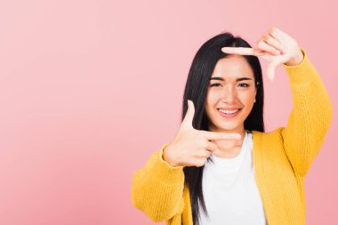 Asyalı güzel mutlu genç kadın fotoğrafçı gülümsüyor. Fotoğraf için ön yüz hareketi yapıyor. Pembe arka planda izole edilmiş stüdyo çekimi.