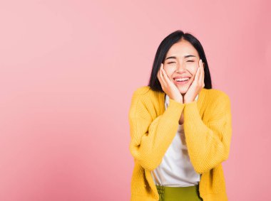 Mutlu bir Asyalı portresi. Yanaklarını tutarak gülümseyen güzel bir kadın. Pembe arka planda izole edilmiş kamera stüdyosuna bakıyor.