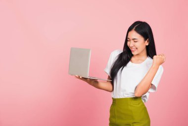 Mutlu Asyalı güzel bir genç kadının portresi dizüstü bilgisayarla gülümseyen ve başarıyı kutlayan heyecanlı bir gülümseme, pembe arka planda izole edilmiş bir stüdyo çekimi,