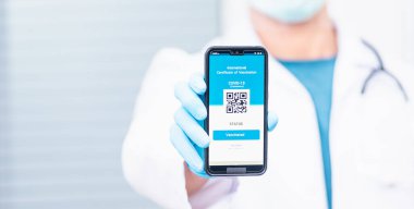 Tıbbi maskeli doktor uygulama akıllı telefon dijital aşılı pasaport coronavirüsü (COVID-19) sertifikası gösteriyor.