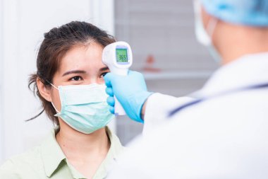 Doktor, hastanede güvenlik, ilaç ve sağlık hizmetleri konsepti için COVID-19 (koronavirüs) belirtileri için hastanın vücut sıcaklığını ölçen kızılötesi alın termometresi tabancası kullanıyor.