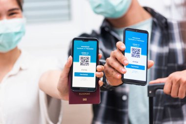 Koronavirüs salgını sırasında akıllı telefon ekranında dijital aşı sağlık pasaport uygulamasını gösteren Asyalı genç kadın ve erkek seyahat etmeye hazır.