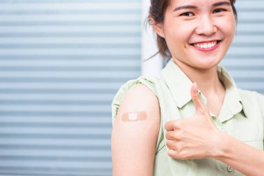 Koronavirüs Covid-19 aşısı aşısı sonrası kolunda yara bandı olan, el hareketi yapan genç bir Asyalı kadın, Coronavirus COVID-19 aşı konsepti.