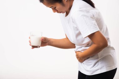 Yakından genç bir kadın hoşgörüsüz, cam sütle el ele tutuşuyor, midesi ağrıyor, laktoza dayanıksızlığı var süt ürünleriyle ilgili sağlıksız bir sorunu var, beyaz arka planda izole edilmiş bir stüdyo çekimi.