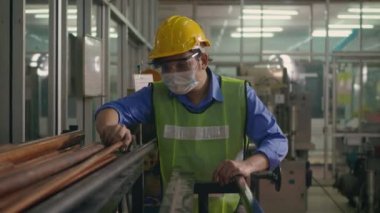 Korumalı kask üniforması giyen Asyalı fabrika işçisi veya mühendis üretim endüstrisinin deposundaki çelik boru malzemelerine bakın.