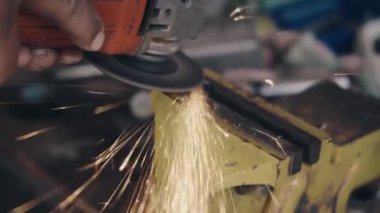 Elektrikli tekerlek kullanan işçi mengenedeki çelik yapıyı öğütüyor ve kesiyor üretim fabrikasındaki öğütme çarkından kıvılcım çıkıyor.