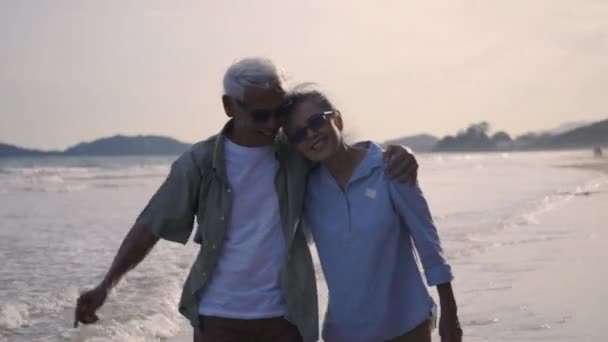 幸せなアジアの高齢者と女性のカップルは 明るい青空とビーチ日当たりの良いから手を取り合って歩くと ロマンチックな高齢者を楽しむ旅行夏休み 退職カップルのコンセプトで生命保険を計画 — ストック動画