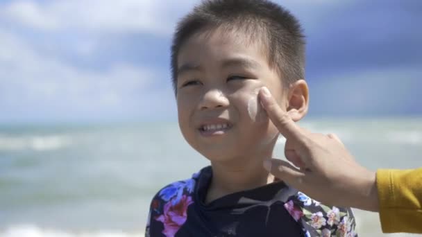 暑假期间 快乐的小男孩站在热带海滩上 在游泳活动之前 幼儿学前班在他的脸上涂了防晒霜紫外线 — 图库视频影像