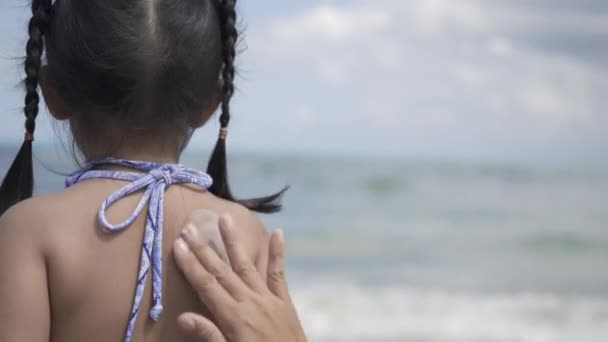 暑假期间 快乐的小女孩站在热带海滩上 幼儿园在游泳活动前给她补上防晒霜紫外线 — 图库视频影像