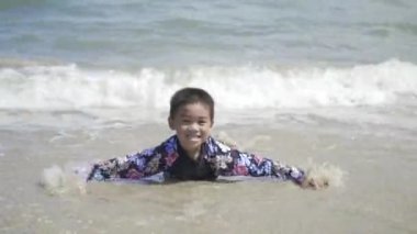 Çok mutlu Asyalı çocuk tropikal plajda su oynuyor neşeli çocuk anaokulunda denizde yüzüyor yaz tatilinde yüzüyor.