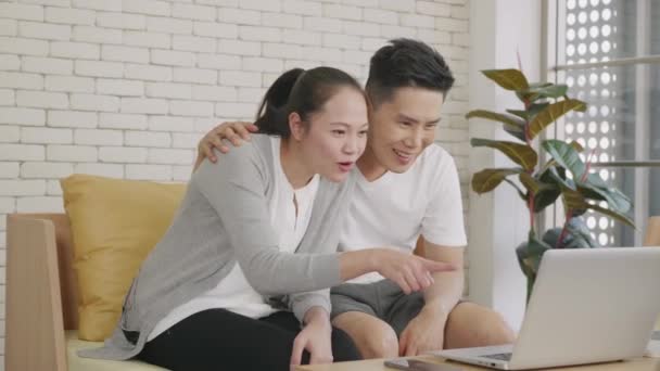 幸せなアジアの家族のカップルの夫と妻は自宅で子供たちにオンラインの社会的距離のビデオ通話を作る話をノートパソコンのコンピュータのウェブカメラ技術を使用してソファに座って笑っている スローモーション — ストック動画