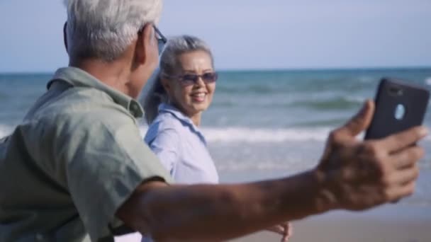 노부부 바닷가를 산책하며 휴식을 취하고 해변에서 스마트폰 셀카를 부부에게 보험을 — 비디오