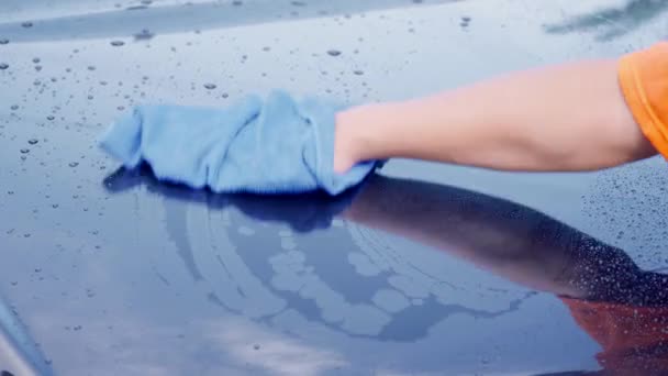 サービスステーションで黒いボンネット車を乾燥させるためにマイクロファイバーワイプ水滴を使用して労働者の手 車のケア洗浄きれいなサービスコンセプト — ストック動画