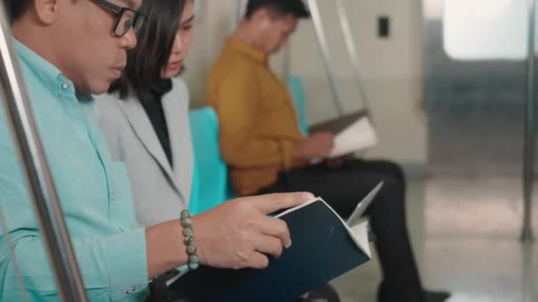 仕事に行く途中の朝に地下鉄の電車の中で一緒に説明を話しているラップトップコンピュータを使って座っている若いアジアのビジネス女性と男性 人々の交通概念 — ストック動画