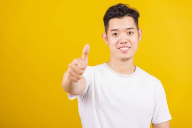 Asyalı yakışıklı genç adam pozitif gülümsüyor. İyi bir hareket gösteriyor. Ya da kameraya bakan bir işaret gibi.