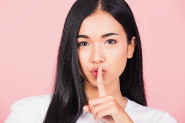 Asyalı mutlu bir portre güzel tatlı bir genç kadın gülümsüyor parmaklarını dudaklarına koyuyor sessiz bir jest stüdyosu çekimleri pembe arka planda izole edilmiş Taylandlı kadın fotokopi çekimleri için kameraya bakıyor.