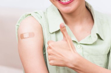 Koronavirüs Covid-19 aşısı aşısı sonrası kolunda yara bandı olan, el hareketi yapan genç bir Asyalı kadın, Coronavirus COVID-19 aşı konsepti.