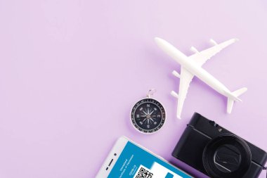 Model uçak, kamera ve dokunulmazlık kartı, mor arka plandaki akıllı telefondan düzenlenmiş uygulama, Covid-19 salgını sırasında seyahat konsepti dijital aşı sertifikası konsepti