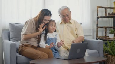 Mutlu aile büyükbabası, kızı ve torunu internette görüntülü konuşma yapıyorlar. Babasıyla dizüstü bilgisayar kullanıyorlar. Yaşlı büyükbaba, küçük torunu ve annesini evinde kucaklıyor.