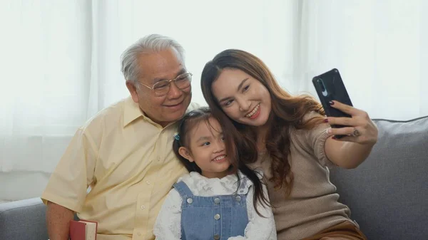 快乐的家庭时光 亚洲祖父母笑着拿着自己的孙女在沙发上用手机在家里 老年人或爷爷 女儿和女孩一起住在客厅里 — 图库照片