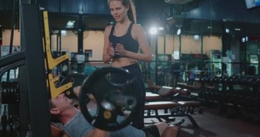 Kişisel antrenör ağırlık kaldırmada ağırlık kaldırmada yardımcı oluyor halter esneme kaslarıyla kadın jimnastik yapan erkeği eğitiyor spor formundaki vücut geliştirme konsepti.
