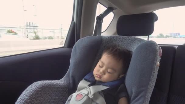 アジアの小さな赤ちゃん男の子は車の中で寝ています安全チャイルドシート上の車の中で道路上の旅行に行く中に — ストック動画