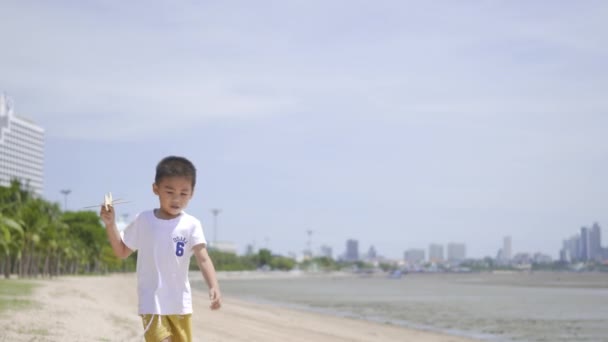 快乐的小男孩在热带海滩玩玩具飞机在暑假旅行 有趣的小男孩坐着飞机在海滨跑来跑去 — 图库视频影像