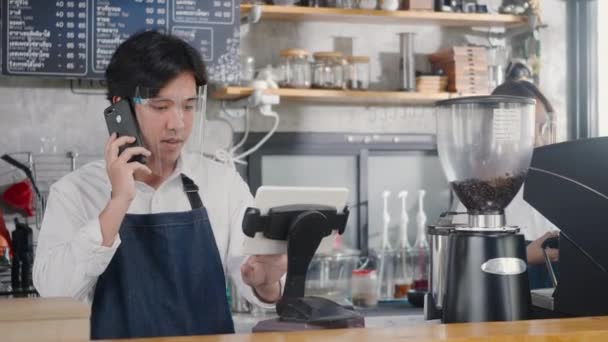 ハッピーアジアバリスタ男コーヒーメーカーは コーヒーカフェショップ マネージャーサービスの小さなビジネスコンセプトでコンピュータへの電話とレコード事前注文を受け取ります — ストック動画