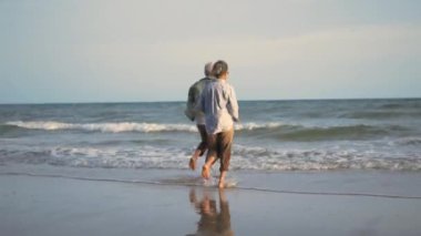 Mutlu Asyalı üst düzey erkek ve kadın çiftler kumsala koşar ve eğlenceli, romantik yaşlılar yaz tatilinin tadını çıkarırlar. Emekliler konseptinde hayat sigortası planlarlar.