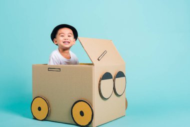 Mutlu Asyalı çocuk araba sürerken gülümse. Karton kutu hayal gücü, yaz tatili seyahat konsepti, mavi arkaplanda metin alanı için fotokopi alanı olan bir stüdyo.