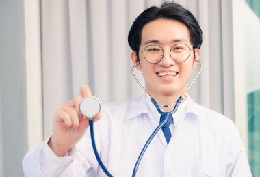 Mutlu Asyalı genç doktor portresi üniformalı gülümseyen yakışıklı adam ve steteskop, sağlık sigortası konseptini gösteriyor.