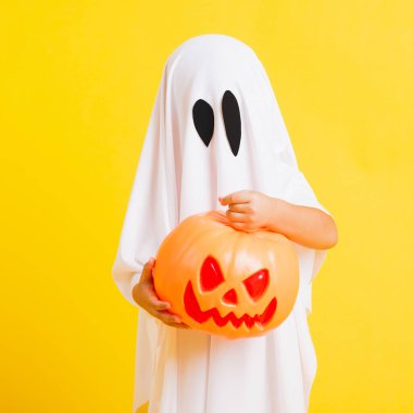Komik cadılar bayramı çocuğu kavramı, beyaz kostümlü şirin çocuk Cadılar Bayramı hayaleti korkunç elinde turuncu kabak hayaleti, beyaz arka planda sarı bir stüdyo.