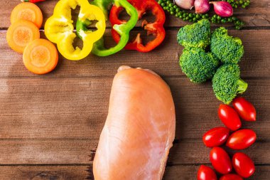 Çiğ tavuk göğsü filetoları pişmemiş ve sebzeli (havuç, domates, Block Kerry, dolma biber, biber, sarımsak) tahta masa arkaplanındaki stüdyo çekimi