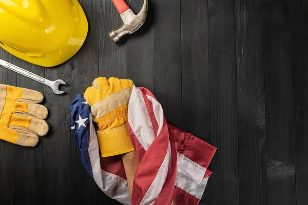 Happy Labor day. Several engineer constructor work tools and , glove holding gripping US American flag with copy space on black dark background, Made in USA, American workforce concept