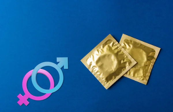 World sexual health or Aids day, Top view flat lay condom in wrapper pack and Male, female gender signs, studio shot isolated on a dark blue background, Safe sex and reproductive health concept