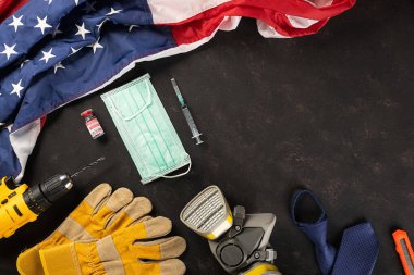 Mutlu İşçi Bayramı. Birçok mühendis çalışma araçları, tıbbi yüz maskesi koruyucu ve kopya alanı siyah arkaplanı olan Amerikan bayrağı, patlak koronavirüs konsepti sırasında Amerikan işgücü