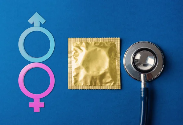 World sexual health or Aids day, flat lay medical equipment, condom in pack, stethoscope and Male, female gender signs, studio shot isolated on dark blue background, Safe sex reproductive health